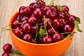 Fresh ripe cherries overflowing in an orange bowl on a wooden surface