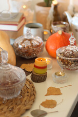 Lit candles, cookies, chocolate, nuts, tea, wine, pumpkins, books, reading glasses and autumn leaves on the table. Autumnal hygge at home. Selective focus.