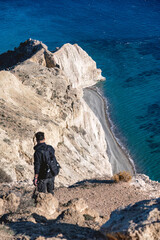 Photographer hiking white limestone cliffs of pissouri, carrying backpack, overlooking azure mediterranean waters under bright sunlight