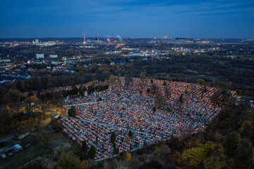 Cemetery on All Saints Day evening with glowing candles and lanterns illuminating graves, warm light reflecting on tombstones creating peaceful atmosphere of remembrance and tradition