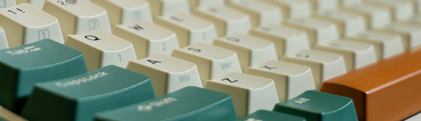 Macro shot of beige and green keyboard keys with orange Enter key, focus on middle row letters, front and back softly blurred for a shallow depth of field.