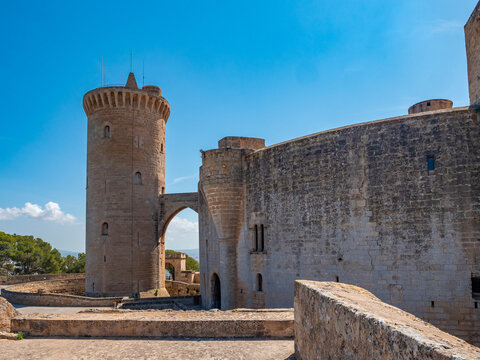 Castell de Bellver, Palma de Mallorca, historic stone castle with a tall cylindrical tower and an arched gateway stands under a clear blue sky, Majorca