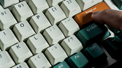 Finger pressing orange Enter key on mechanical keyboard, detailed macro focus on key surface and fingertip texture, surrounding keys softly blurred.
