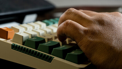 Close-up of a hand pressing keys on a mechanical keyboard with green and orange keycaps, showing sharp focus on fingers while the background keys are softly blurred.