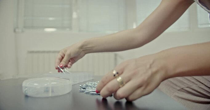 Person meticulously sorts small metal screws into compartments of a plastic storage box. This video features clear audio, creating a peaceful and immersive sensory experience with home items.