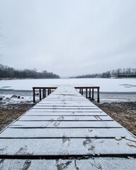 Wooden pier on frozen lake (symmetric diminishing perspective view). Winter morning scene with snow-covered ice on the water,footsteps on the boardwalk.