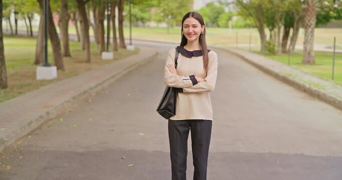 Indian happy young adult gen z proud smart lady female look camera cross arms standing outdoor campus area. Teen age pupil pretty girl fold hand wear bag staring cam do casual pose enjoy new day place