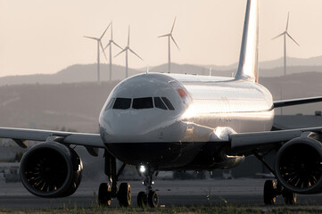 Naklejka premium Modern airplane on runway with wind turbines in background. Larnaca Airport, Cyprus