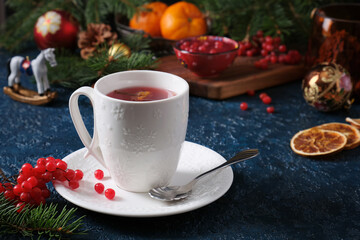 A beautiful white cup with New Year symbols and tea against a table decorated with New Year branches and cranberries.