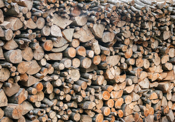 Tall long stack of cut firewood logs of various thickness neatly piled together