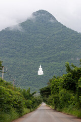 Scenic Serenity: An imposing peak, shrouded in mist, majestically frames a serene, off-the-beaten-path road, leading towards a monument of tranquility and reverence.