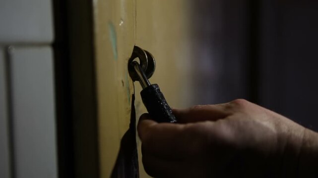 An unknown man wants to break into a closed door and shines a flashlight on the padlock.