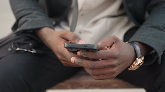 Hands holding smartphone beside laptop bag placed near thighs, highlighting casual modern style, focus on hand watch, human gesture, and technology connection expressed through balance