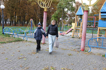 A woman and her son are walking home after a pleasant walk in the autumn park.