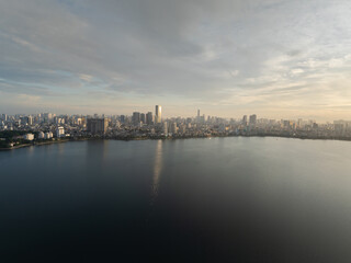 Fototapeta premium Expansive view of West Lake at sunrise with soft light reflecting on calm water and distant city skyline.