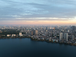 Fototapeta premium Aerial cityscape of Hanoi beside West Lake during sunrise with soft blue and pink tones in the sky.