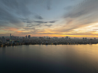 Fototapeta premium Colorful sunrise over West Lake with city skyline and shimmering reflections on calm water.
