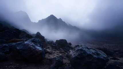 Dramatic mountain landscape shrouded in thick fog and mist with rugged rocky terrain in the foreground