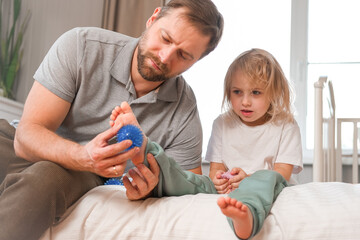Father using a spiky massage ball for daughter to relieve muscle tension, aid recovery after...