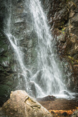 Close-up of fresh mountain waterfall hitting the rocks in a narrow gorge. Clear stream and textured cliff face in a wild, tranquil setting