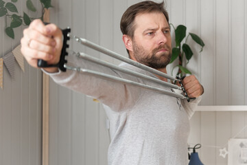 Mature man using metal spring chest expander pull exercises, upper body muscles, forearms and grip. Resistance Band. Wellness. 40s Male training neck and shoulder stretch at home for good posture.