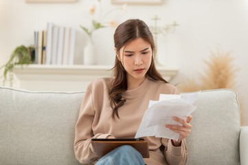 Asian woman feeling unhappy after looking at the bill feels stressed having financial problem, check finances, experiencing lack of money pay for loan, huge taxes, utility rates, get eviction notice