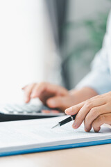 Concept of financial planning and accounting. A businesswoman uses a calculator to analyze reports and charts, calculating budget and investment strategy with focus and precision at office desk.