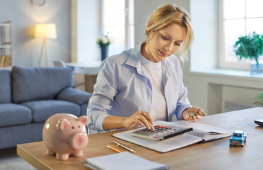 Piggy bank sits on table with woman working at home, using calculator for budget or accounting...