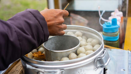 Close-up of a street food vendor preparing hot meatballs (bakso) from a steaming pot at a traditional food cart, capturing authentic Indonesian street culinary culture.