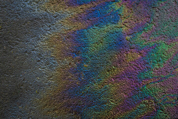 Colorful oil spill on wet asphalt creates vibrant rainbow texture with shimmering light reflections. Concept of environmental pollution and abstract colorful background
