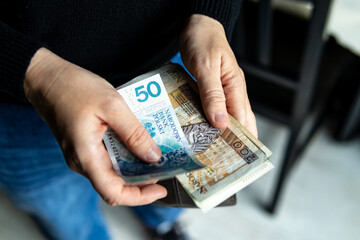 Close-up of hands holding Polish banknotes – 200 and 50 złoty bills. Personal finance, cash transaction or budgeting concept.