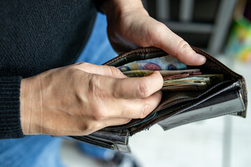 Close-up of a person’s hands opening a wallet filled with Polish banknotes. Concept of cash savings, personal finance or payment.
