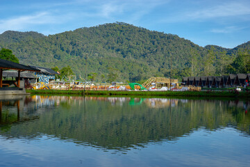 Panoramic view of a calm lake perfectly reflecting the lush green forested mountain and row of A-frame cabins.