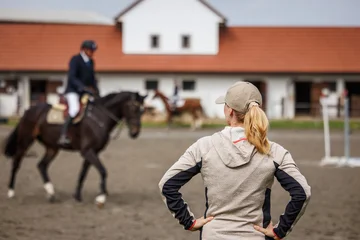 Fotobehang Paardensport Female horse trainer supervising rider training before equestrian show jumping in paddock  © encierro