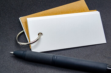 Close up of white banner shape notepad with customizable space for text on black cover background and with black pen.