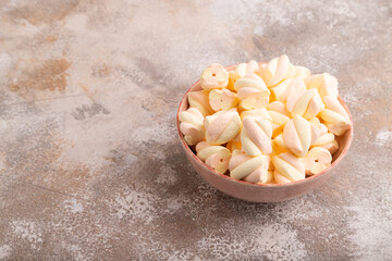 Orange and pink marshmallow in ceramic bowl on brown concrete background, side view, copy space