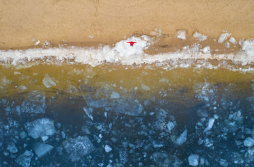 A person in a red jacket making a snow angel on a frozen beach.