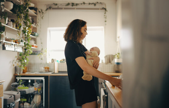 Tired mother holding crying baby while trying to make breakfast - Powered by Adobe