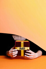 Black Friday gift moment with person holding red present, gold ribbon label, minimalist orange background, inviting party retail illustration for promotional campaigns