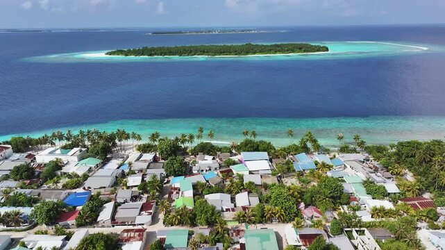 Aerial view of island homes amidst lush greenery, contrasting turquoise and deep blue waters, a serene coastal scene, Maalhos, Baa Atoll, Maldives.