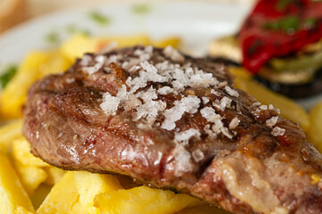 Close-up of grilled pork steak with salt and fries