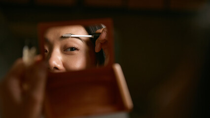 Woman applying eyebrow gel in mirror with precise calm focus. Concept of beauty precision, confidence, and mindful grooming in morning personal care routine.