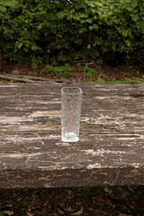 Empty glass vase with a clear embossed pattern, standing on a textured, weathered rustic wooden table. Outdoor scene captured in daylight. Ideal for background and copy space.