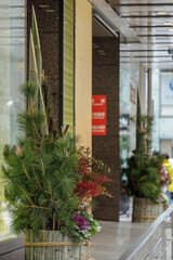 Traditional new year's arrangement, featuring three bamboo stalks of varying height, lush pine branches, berries, and flowering kale, decorates building's entrance during holiday season in Japan.