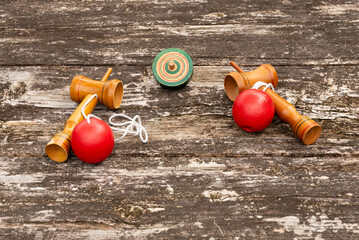 Two Japanese cup-and-ball toys (kendama) and a spinning top (koma), displayed on a weathered rustic wooden table. Symbolizes traditional Japanese games, culture, and nostalgia.