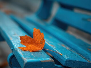 Vibrant Orange Autumn Maple Leaf on Weathered Blue Wooden Bench in Park, Shallow Depth of Field Highlighting Textured Foliage and Rustic Wood Planks