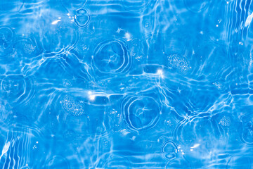 Blue water with ripples on the surface. Defocus blurred transparent blue colored clear calm water surface texture with splashes and bubbles. Water waves with shining pattern texture background.