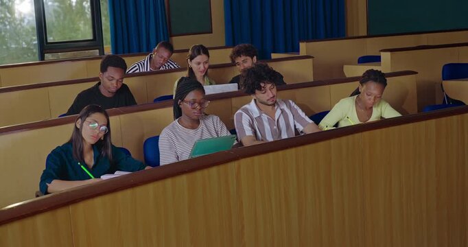 Indian young adult gen z pupil smart girl boy guys sitting desk table hold pencil exam notes book work class room. Teen female learn new study male man talk raise hand share plan ideas day hall place
