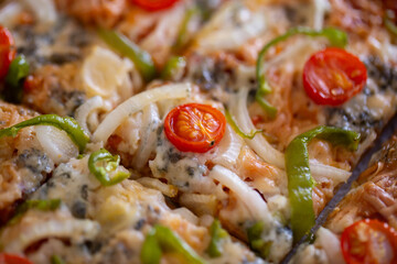 Close-up of pizza with cherry tomato, peppers, onion and roquefort cheese in warm natural light