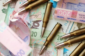 Many rifle bullets lies on lots of ukrainian money bills close up